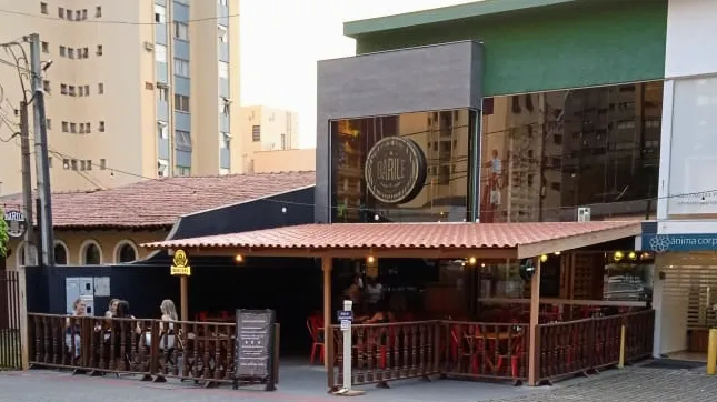 Fachada do Barile Bar vista da rua: varanda coberta de telha, cerca de madeira e mesas com cadeiras vermelhas
