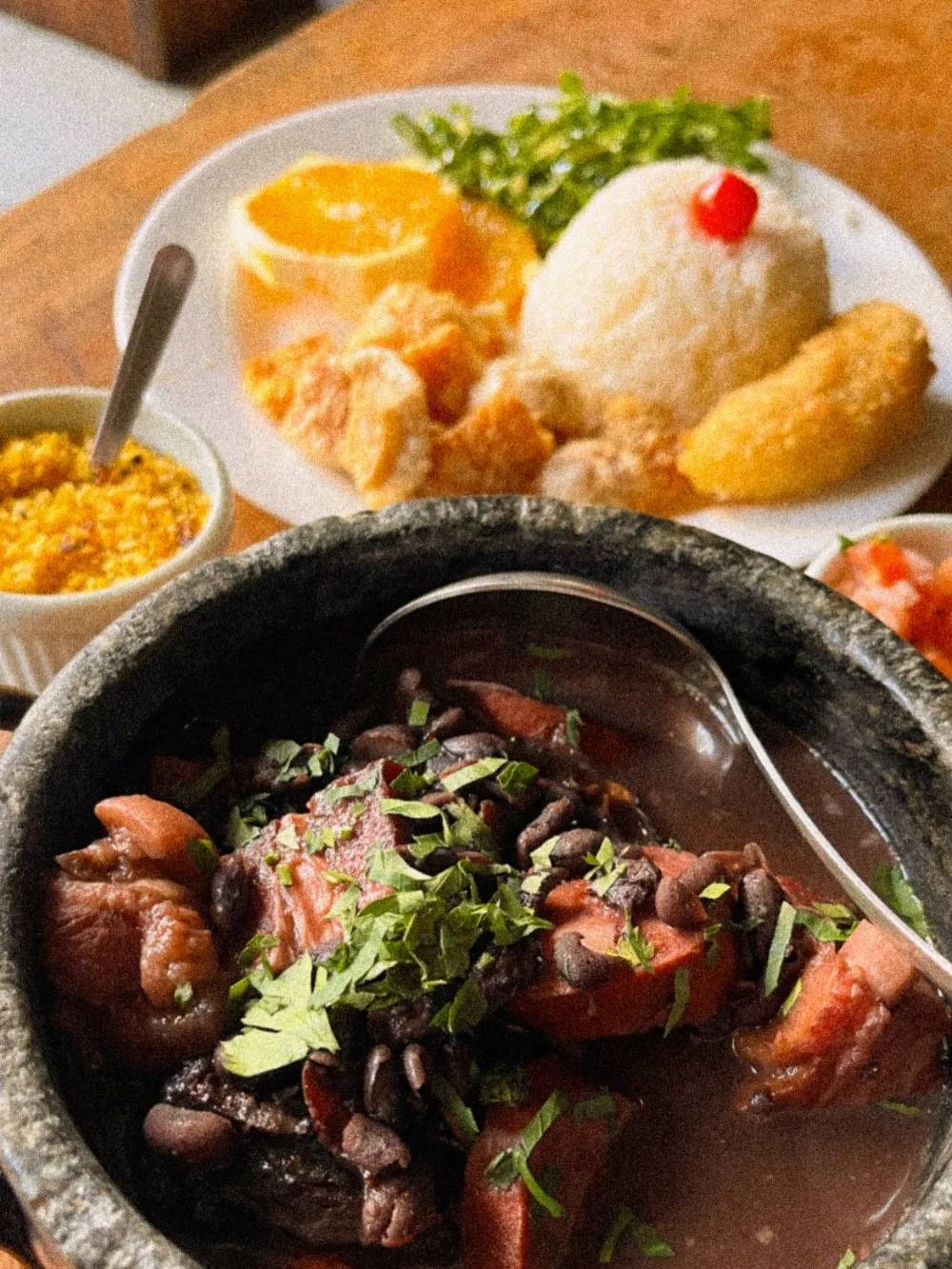 Feijoada servida em panela de pedra, com arroz, torresmo, banana empanada, farofa e laranja